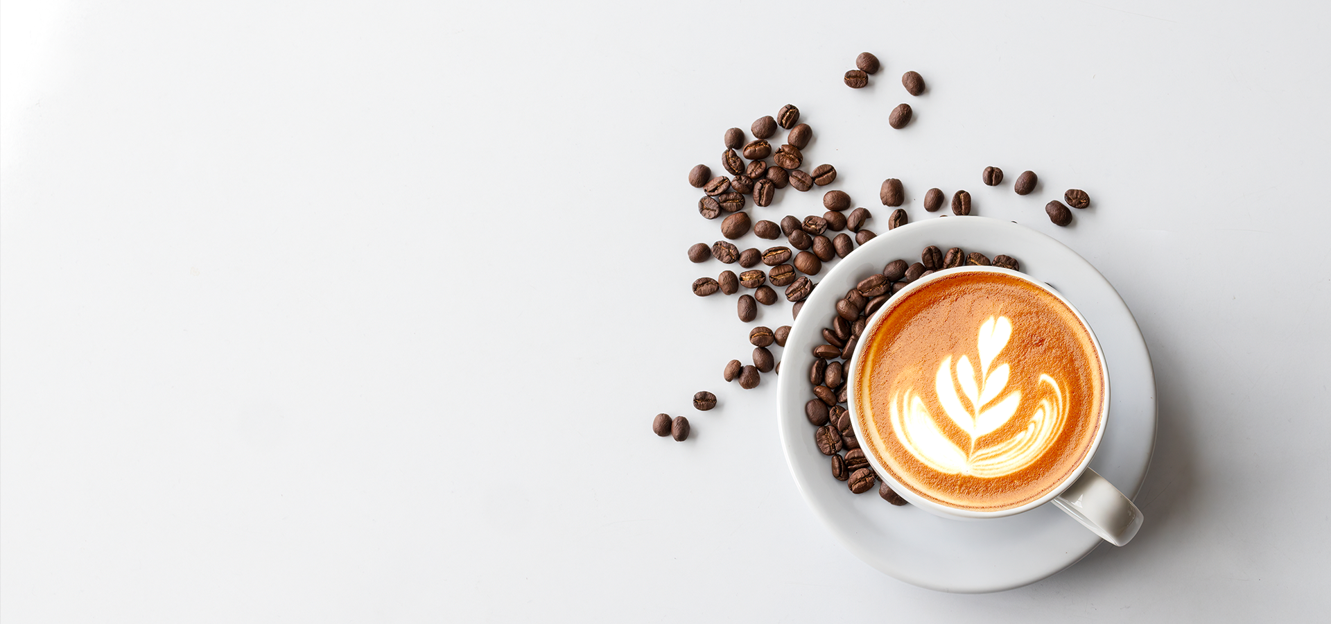 Cup of coffee with latte art and scattered coffee beans on a white background